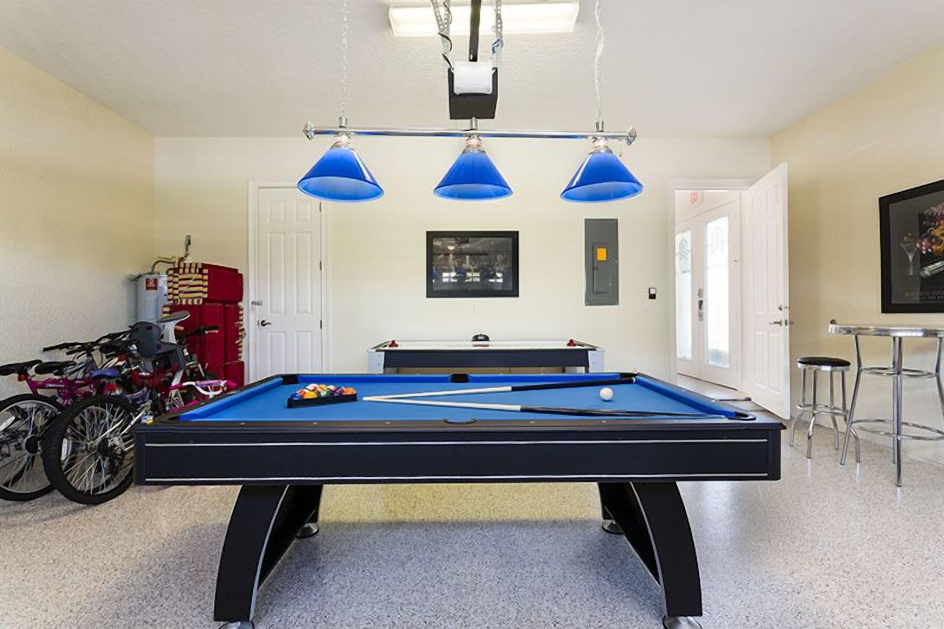 A pool table with three blue lamps overhead, a bicycle rack, and a framed picture on the wall.