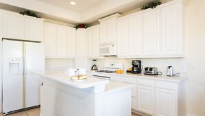 A modern kitchen with white cabinetry, a central island, a refrigerator, a microwave, a coffee maker, and a toaster. - Je47858 - Reunion Resort - 6 Bed 4 Baths Villa (Kissimmee)