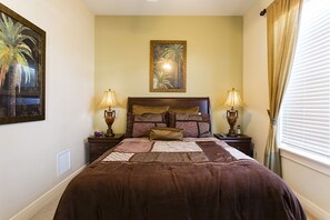 A bedroom with a large bed, two bedside tables with lamps, a headboard with multiple pillows, a framed picture on the wall, and a window with curtains. - Je47858 - Reunion Resort - 6 Bed 4 Baths Villa (Kissimmee)
