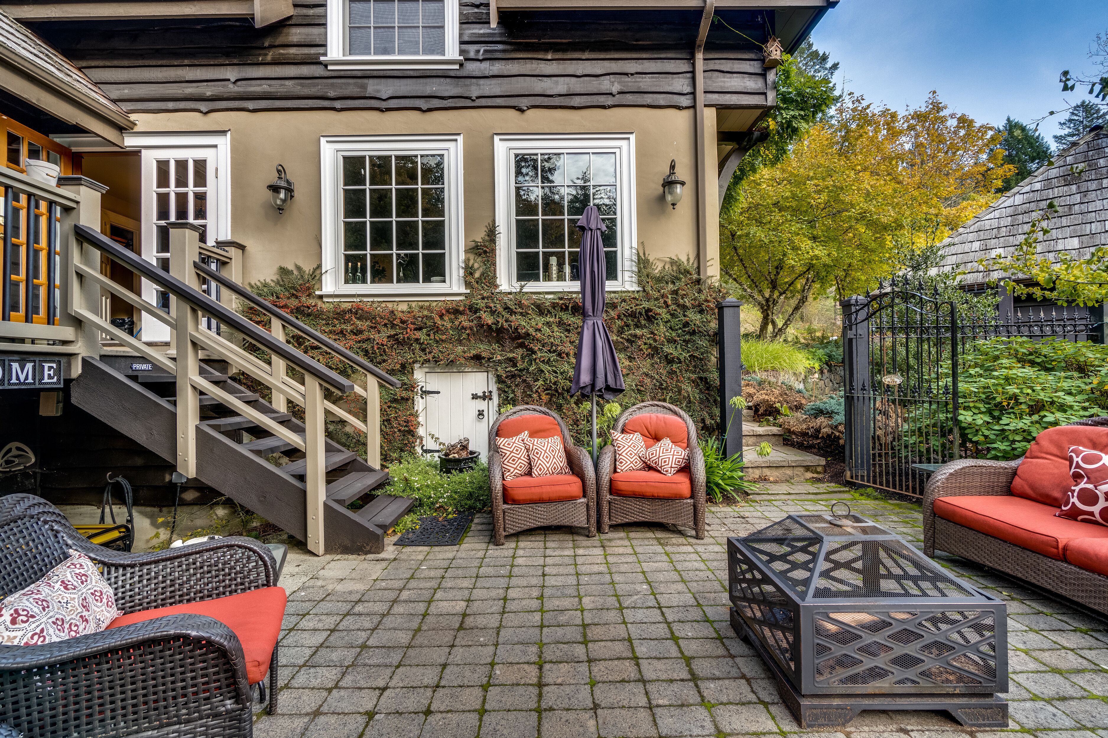 Un espace patio aménagé avec des meubles en osier, une table en métal et un escalier menant à une porte portant l’inscription « ENTRÉE ».