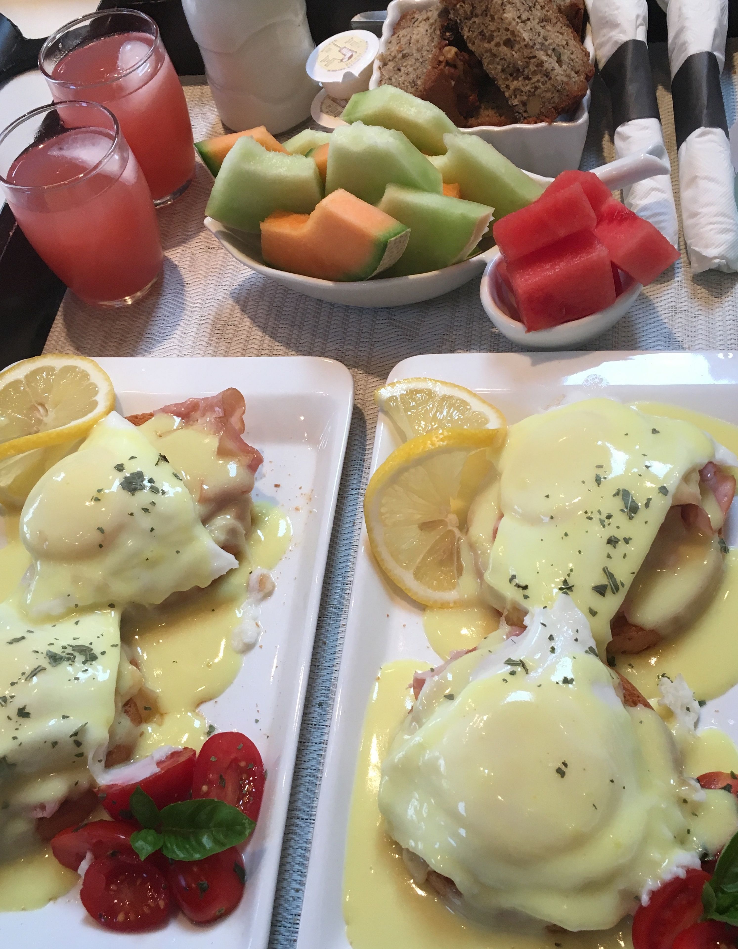 A breakfast setting with eggs benedict, melon, and bread.