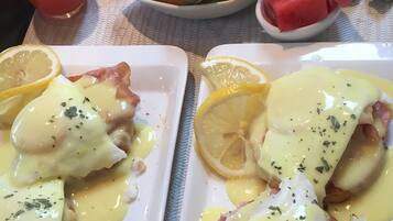 A breakfast setting with eggs benedict, melon, and bread.