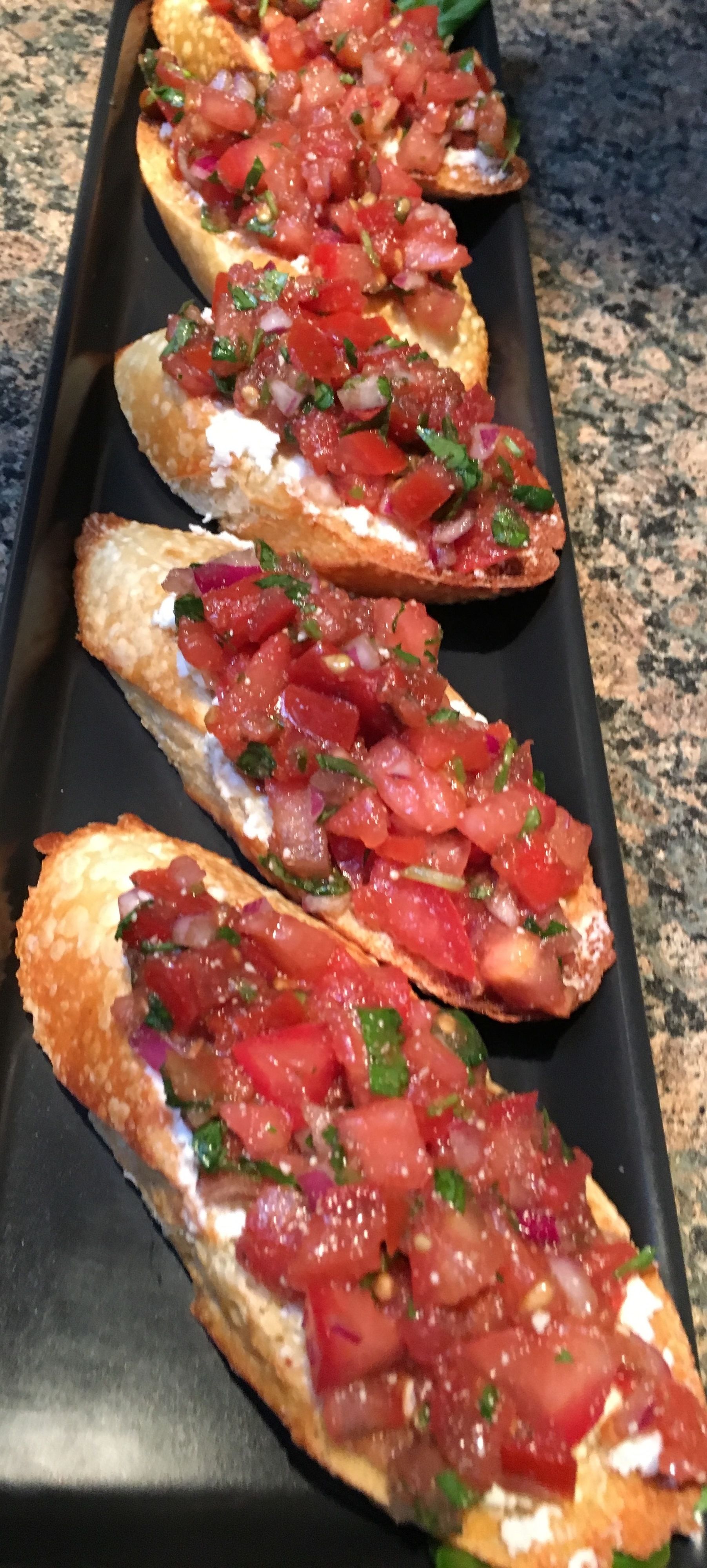 Four pieces of bruschetta on a black tray.