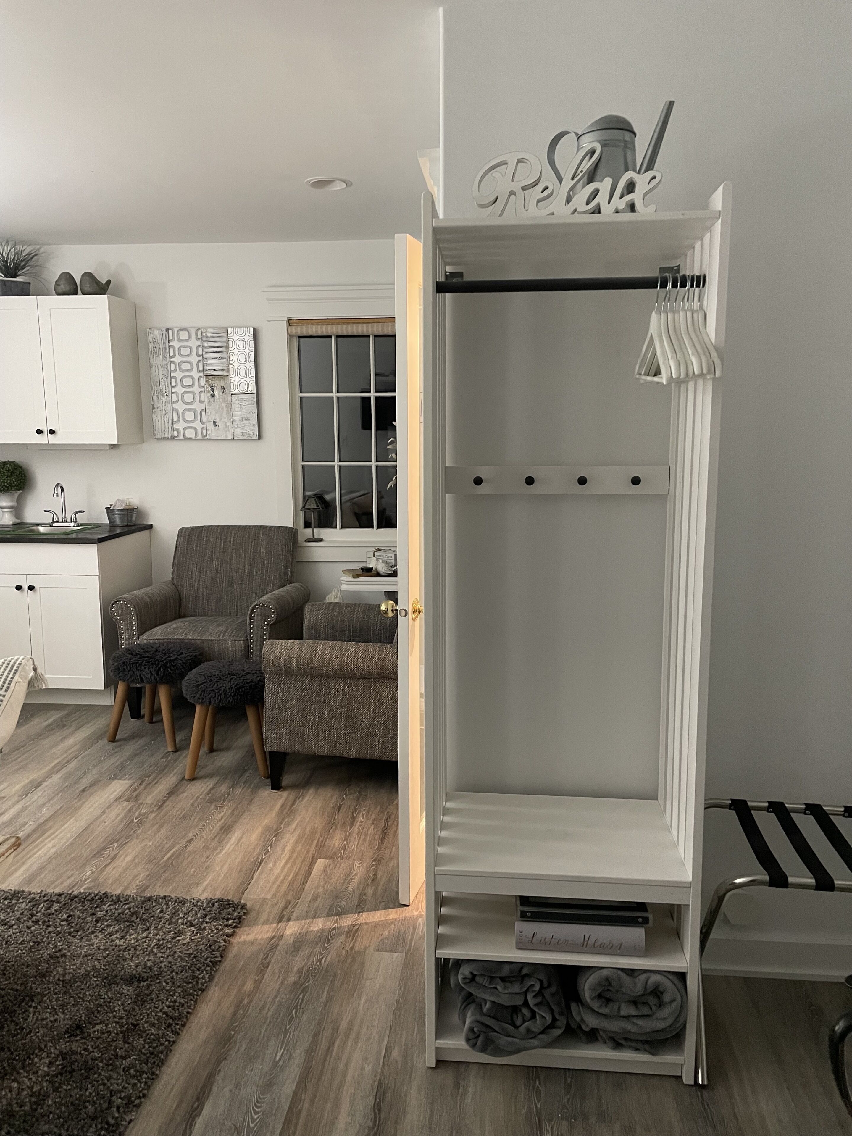 Un dormitorio moderno con un armario blanco, un sillón gris, una mesita pequeña y una ventana con persianas.