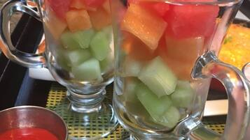 Two clear glasses filled with layered fruit and a small metal cup of red sauce on a tray.