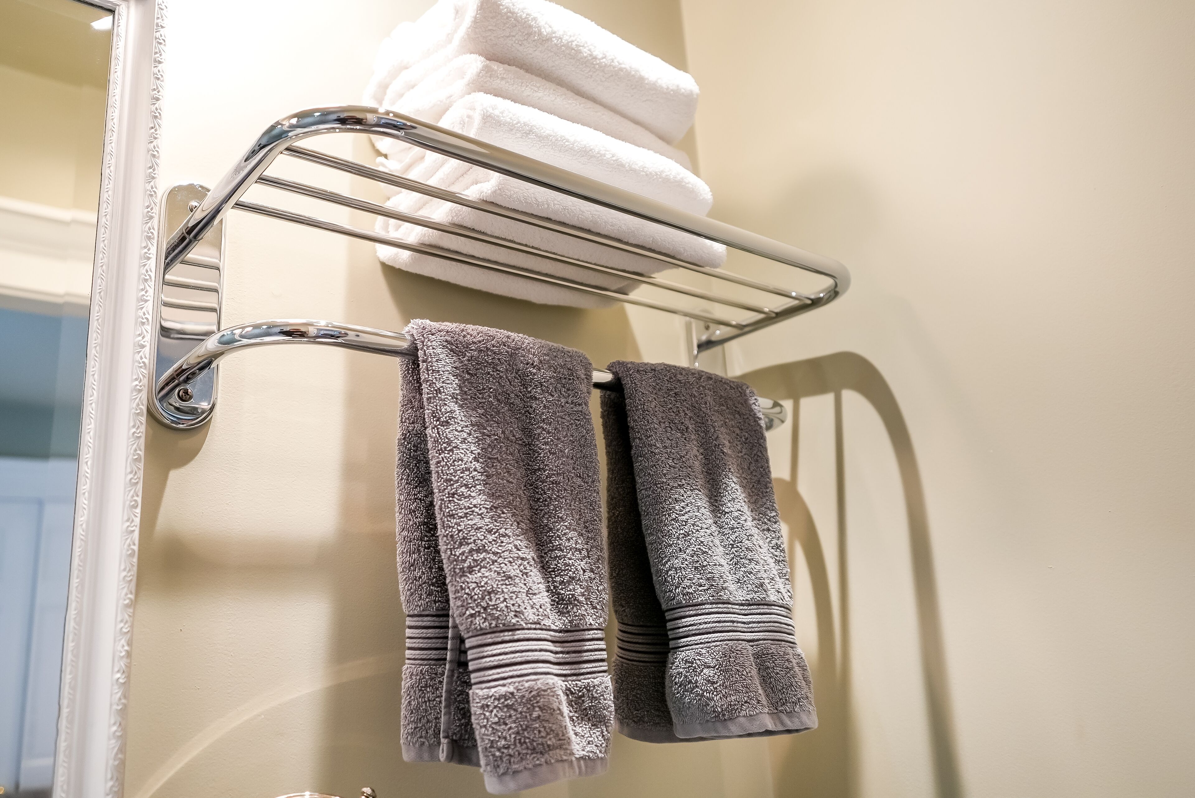 A bathroom with a towel rack holding folded towels and two towels hanging.