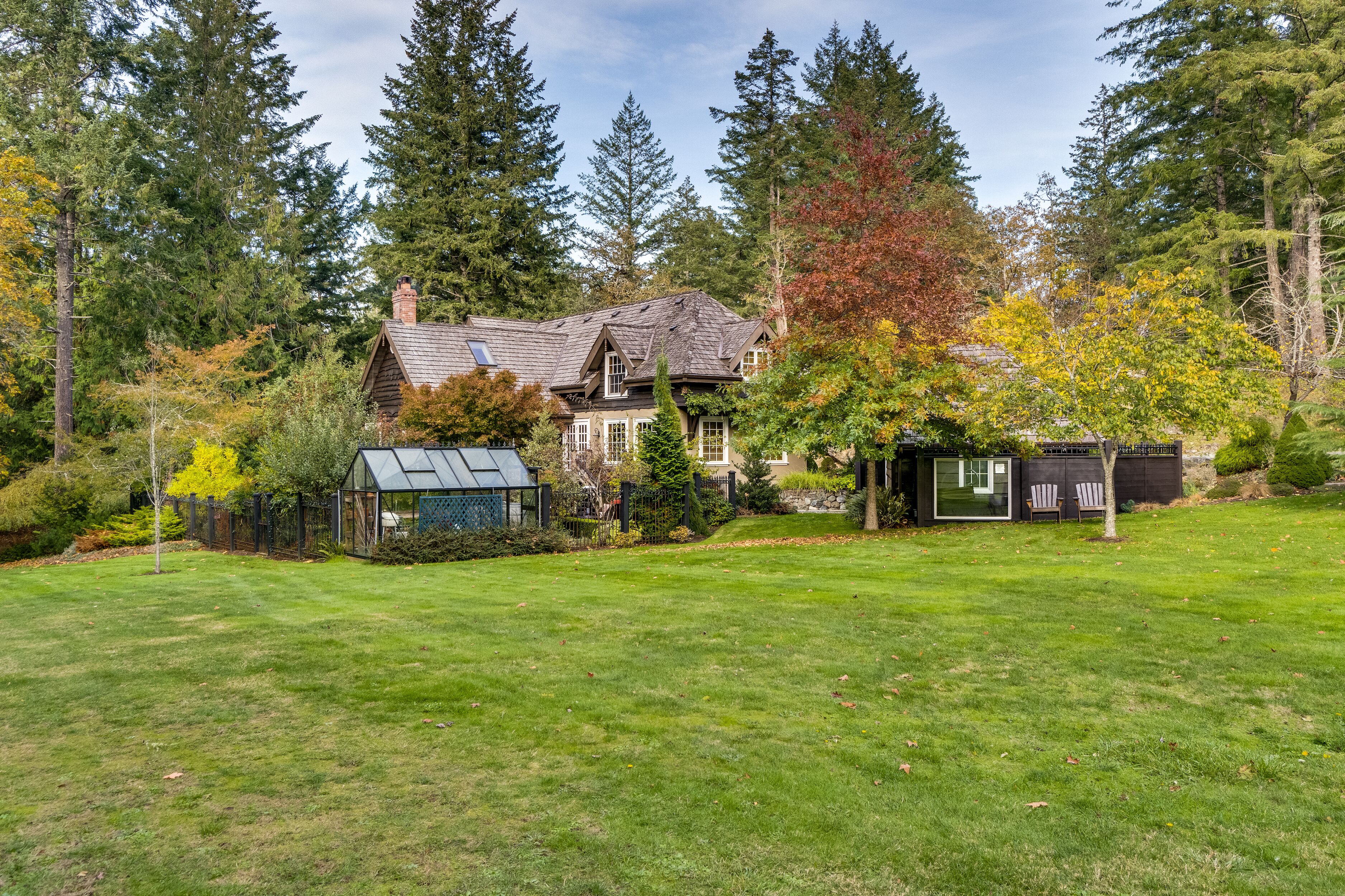 A large house with a well-maintained lawn, surrounded by tall trees and a greenhouse.