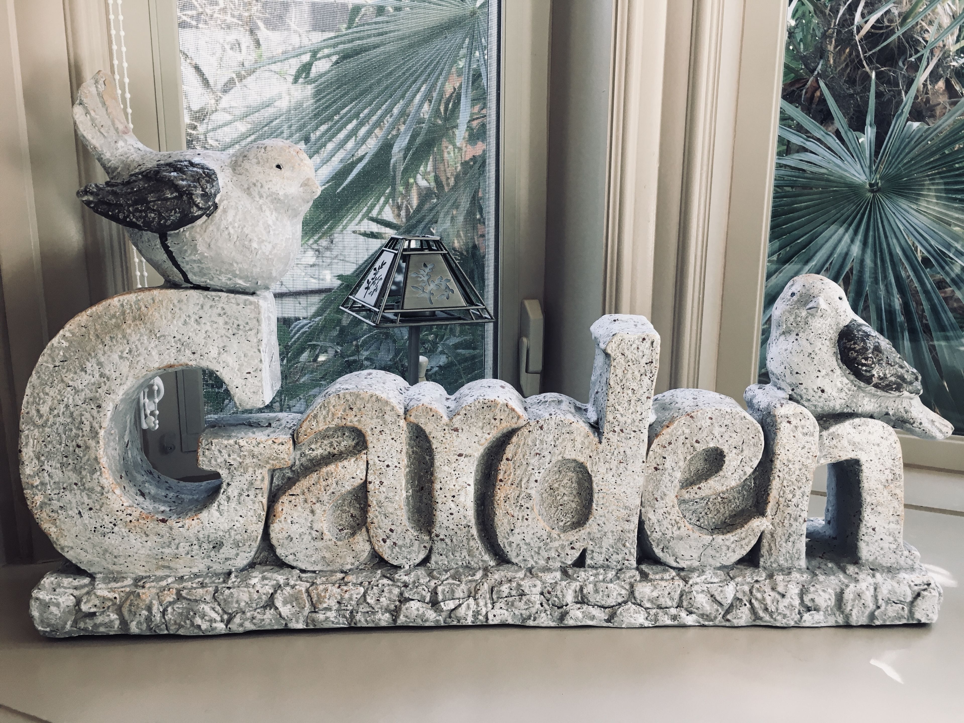 Un letrero decorativo con la palabra 'Garden' y dos pájaros posados encima.