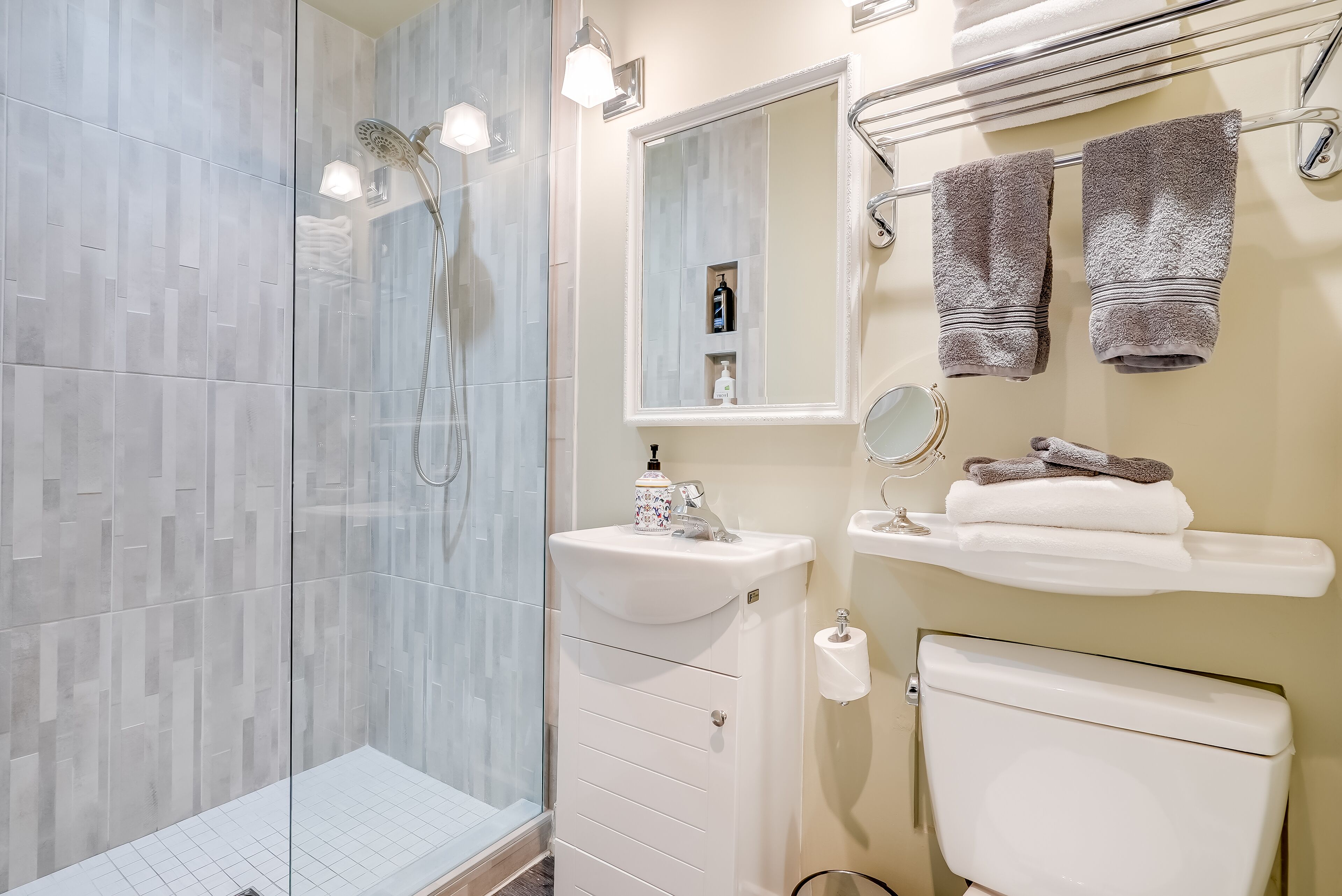 A modern bathroom with a glass shower enclosure, a white sink, a toilet, and a mirror.