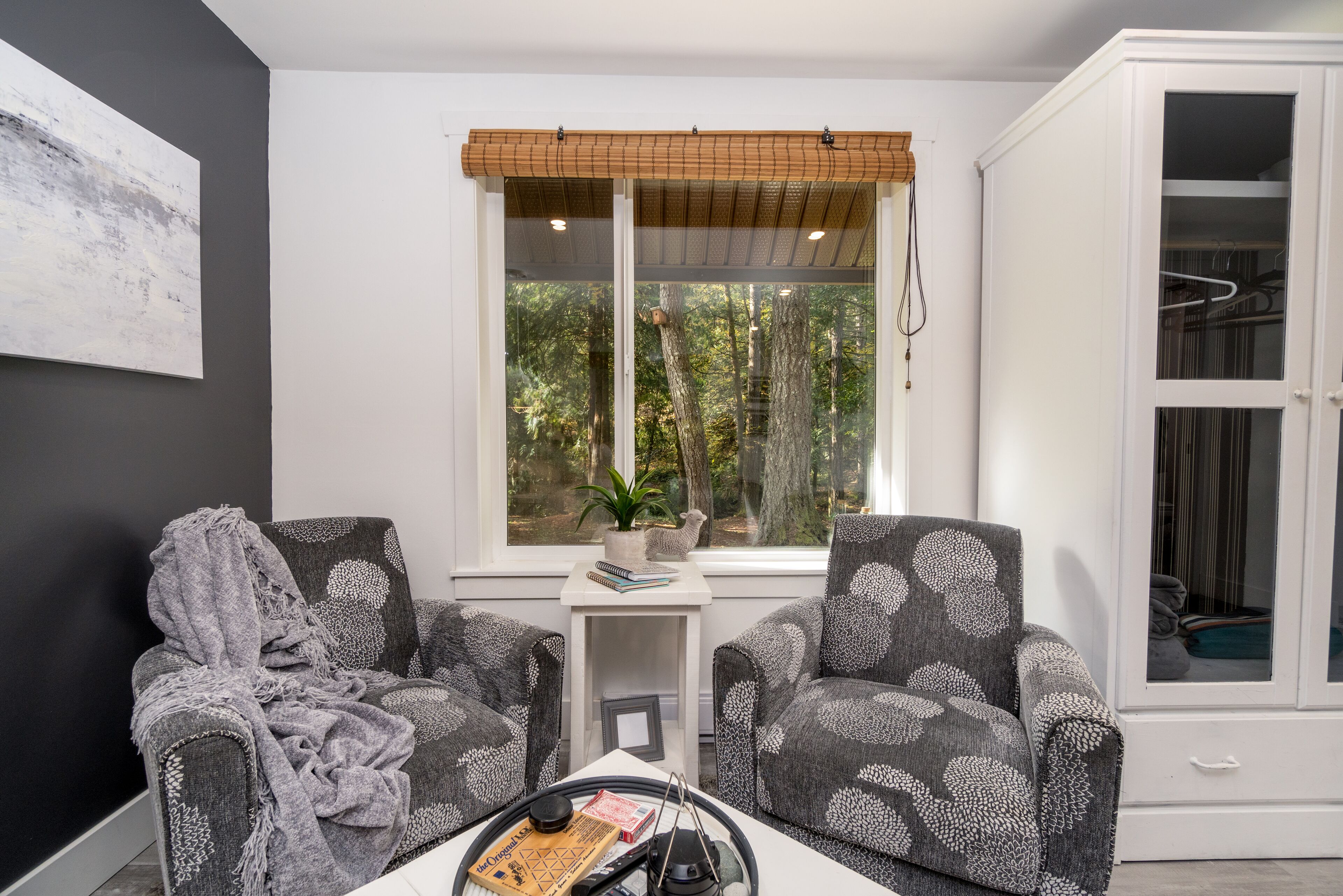 Ein Zimmer mit zwei gemusterten Sesseln, einem kleinen Tisch mit Pflanze und einem Fenster mit Blick auf Bäume.