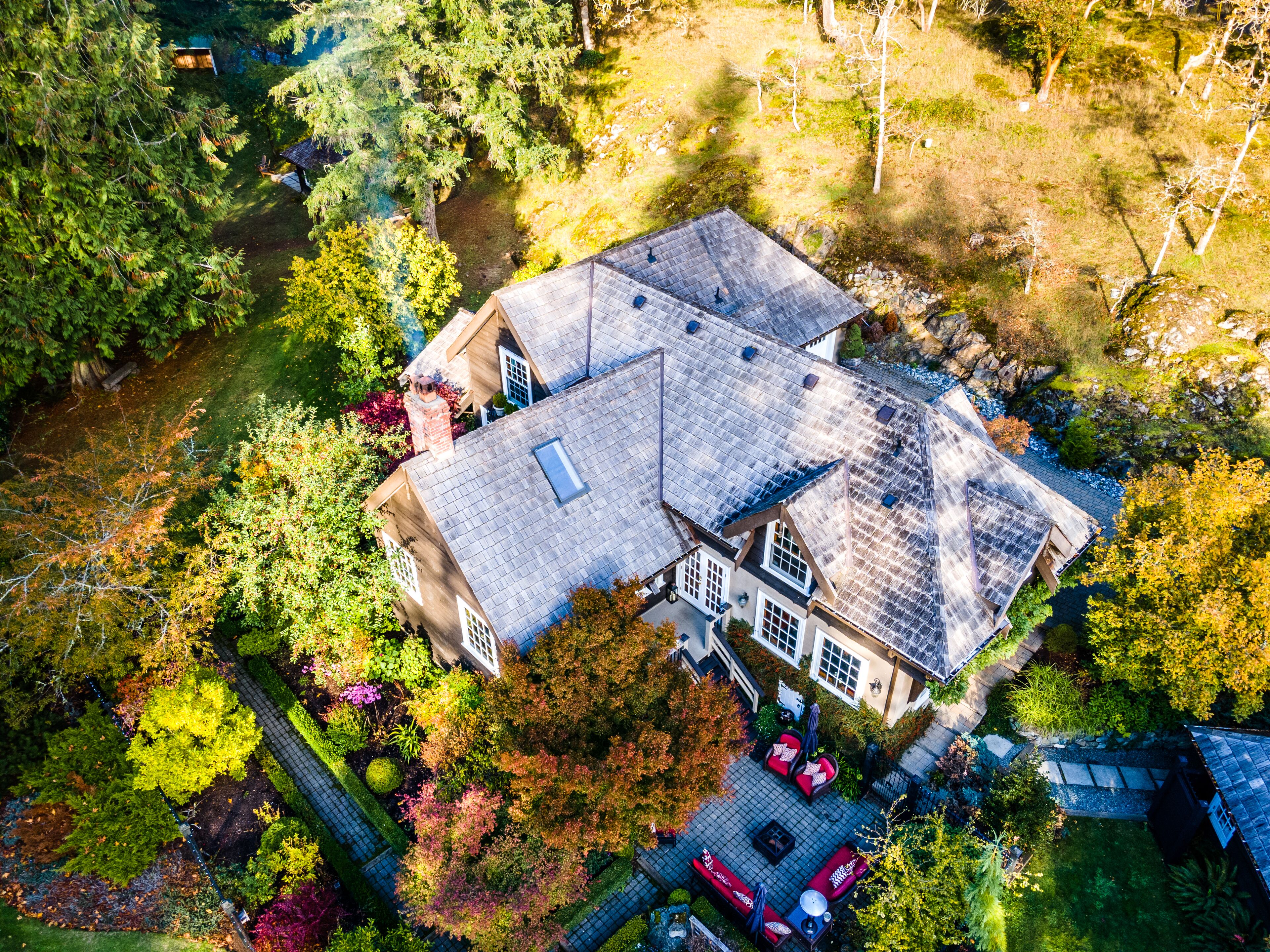 An aerial view of a house with a sloped roof, surrounded by trees and a garden.