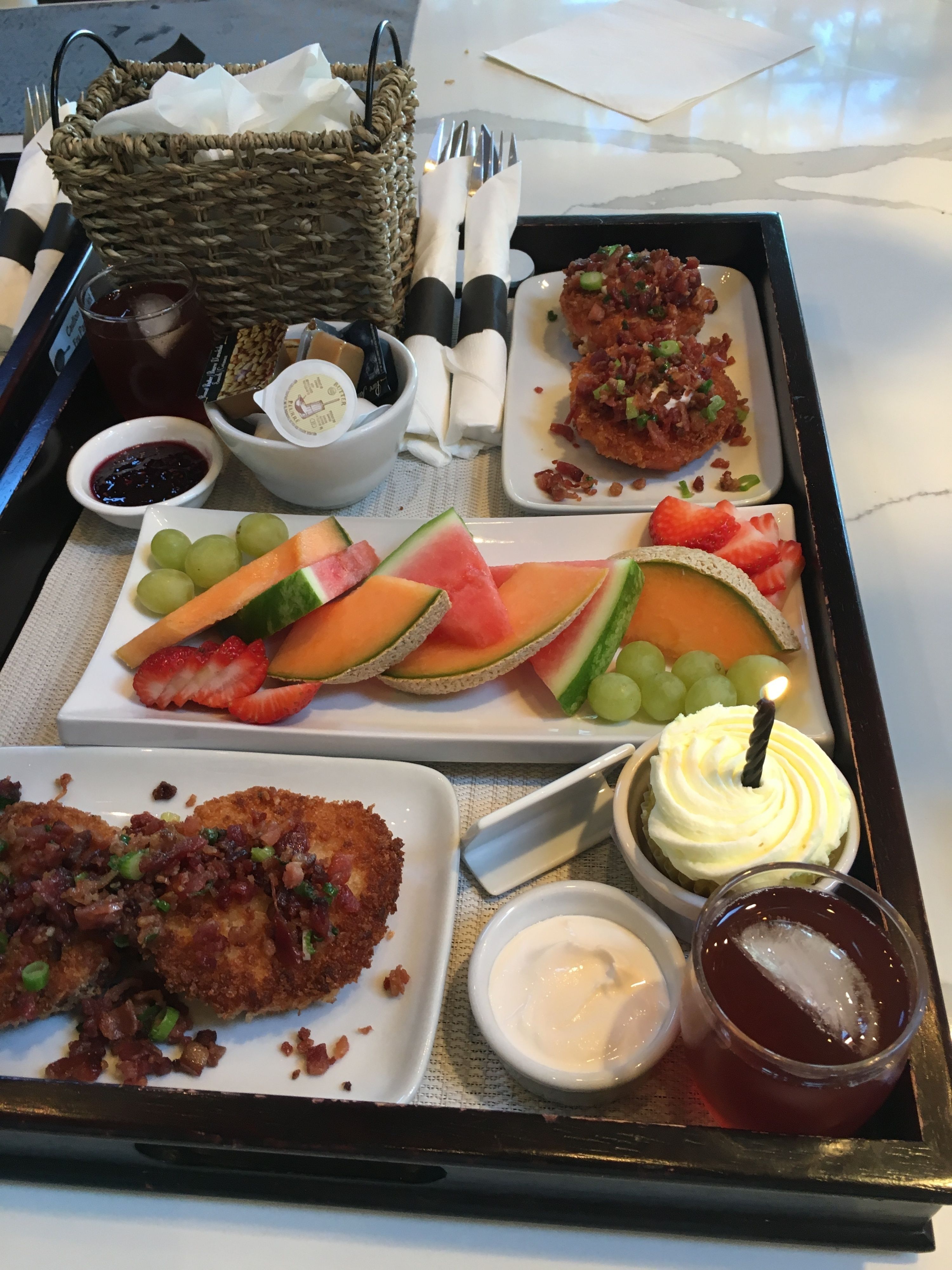 A tray with various food items including breaded meat, fruit slices, and a dessert with a lit candle.