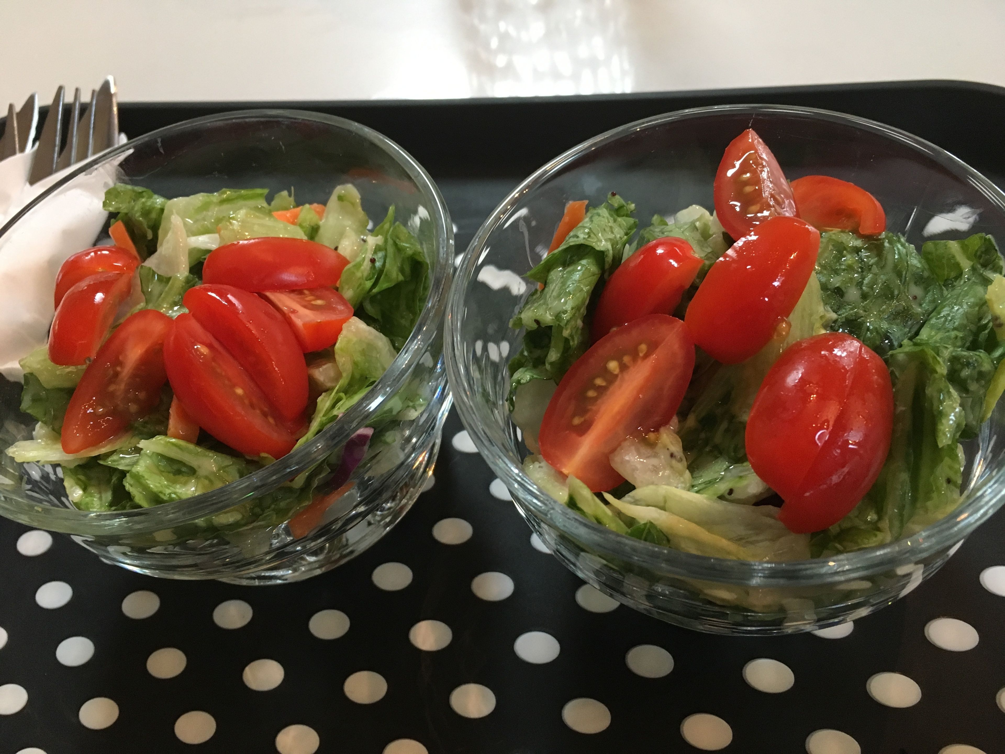 Dos ensaladeras de vidrio con tomates cherry sobre una bandeja negra con lunares blancos.