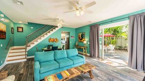 A living room with teal walls, a blue sofa, a wooden coffee table, a staircase, and a view of the outdoors.