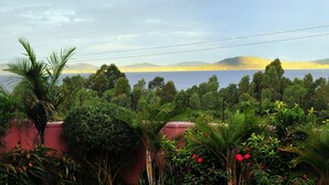 A lush garden with various plants and a view of a lake and distant hills. - Victoria Lake View Guest House & Safaris (Entebbe)