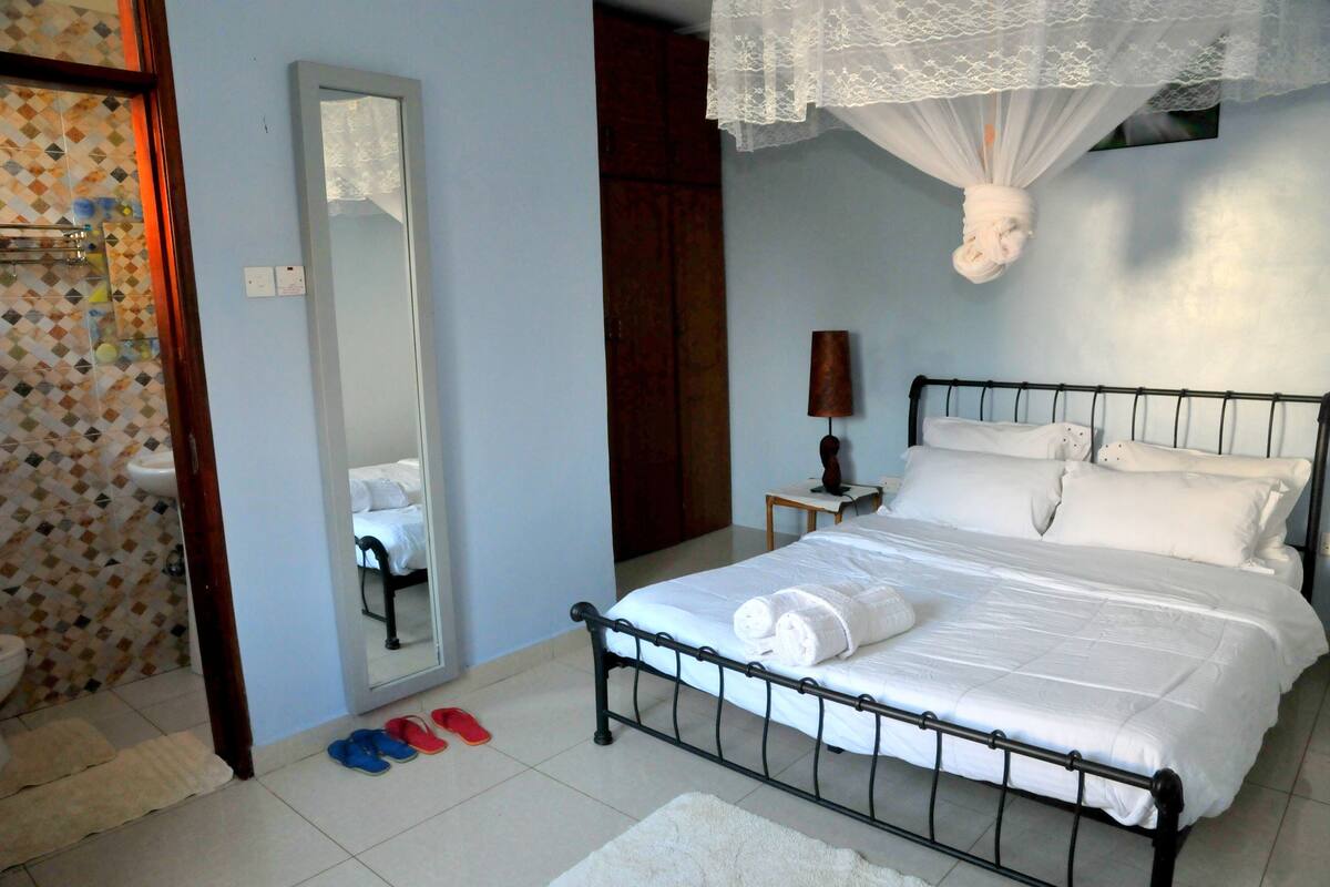 A bedroom with a bed, a mirror, a bedside table, and a hanging light fixture.