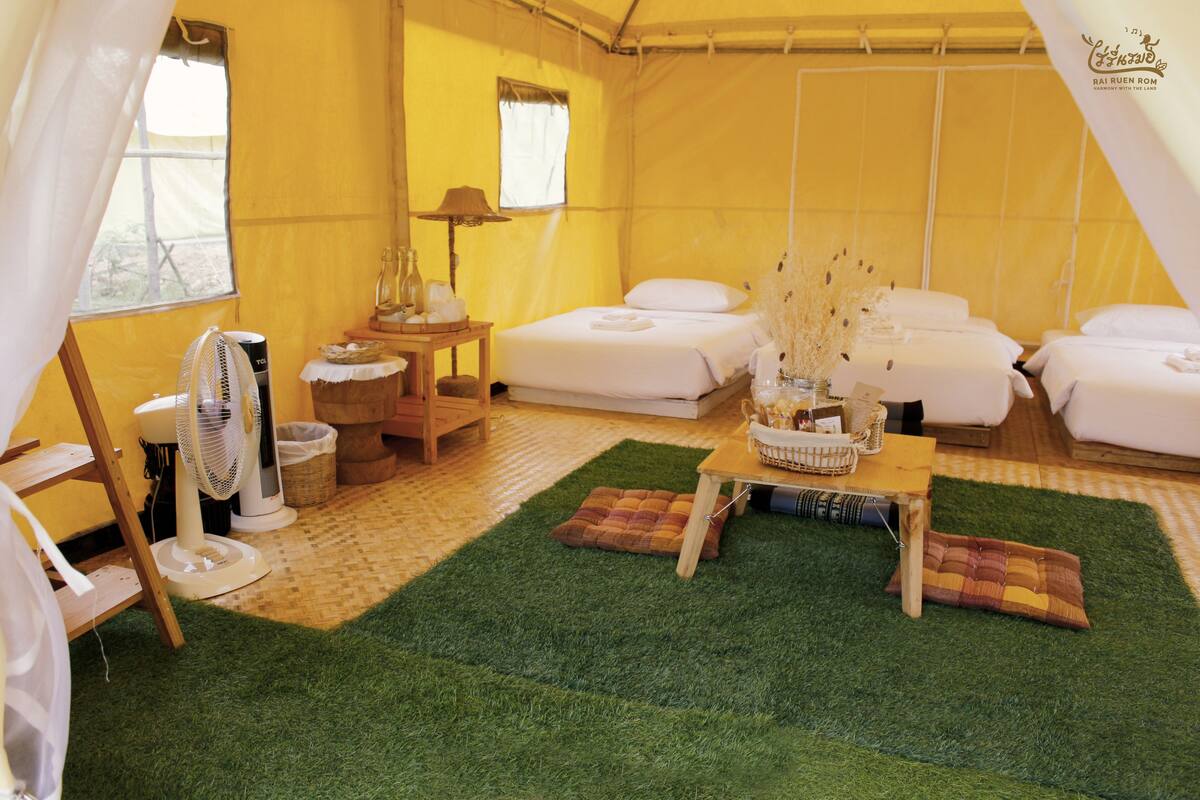 A tented accommodation with multiple beds, a fan, a table with a basket, and a window.