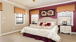 A bedroom with a large bed, two bedside tables, a nightstand, and a ceiling fan.