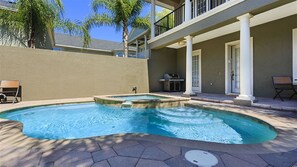 Zwembad met een jacuzzi, omringd door een terras met stoelen en een barbecue.