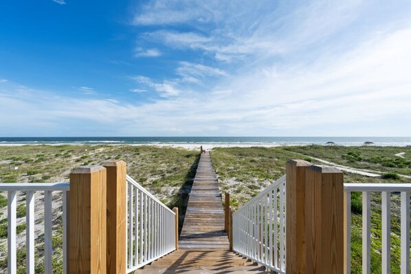 A wooden boardwalk leading to a beach with white railings on both sides.