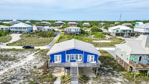 A coastal residential area with a prominent blue house featuring a balcony and a wooden deck leading to the entrance.