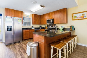 Una cocina con armarios de madera, electrodomésticos de acero inoxidable, encimera de granito y taburetes de bar.
