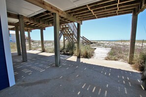 Une maison de plage dotée d’une terrasse en bois, d’un escalier menant à une zone abritée et offrant une vue sur la plage.