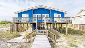 A blue house with a wooden deck and stairs leading to a balcony.