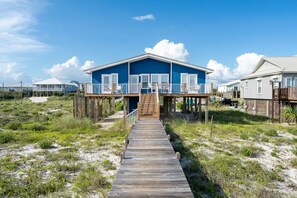 A beachfront property with a wooden walkway leading to a blue house with a balcony.