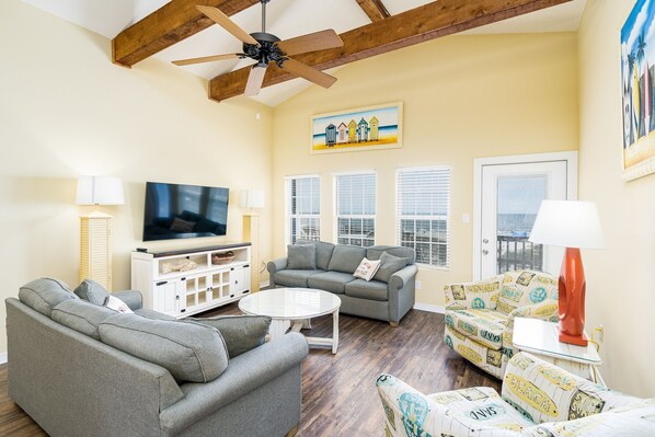 A living room with a sofa, armchairs, a coffee table, a TV, and a ceiling fan.