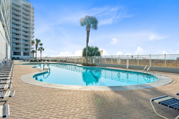 A swimming pool with lounge chairs, palm trees, and a high-rise building in the background.