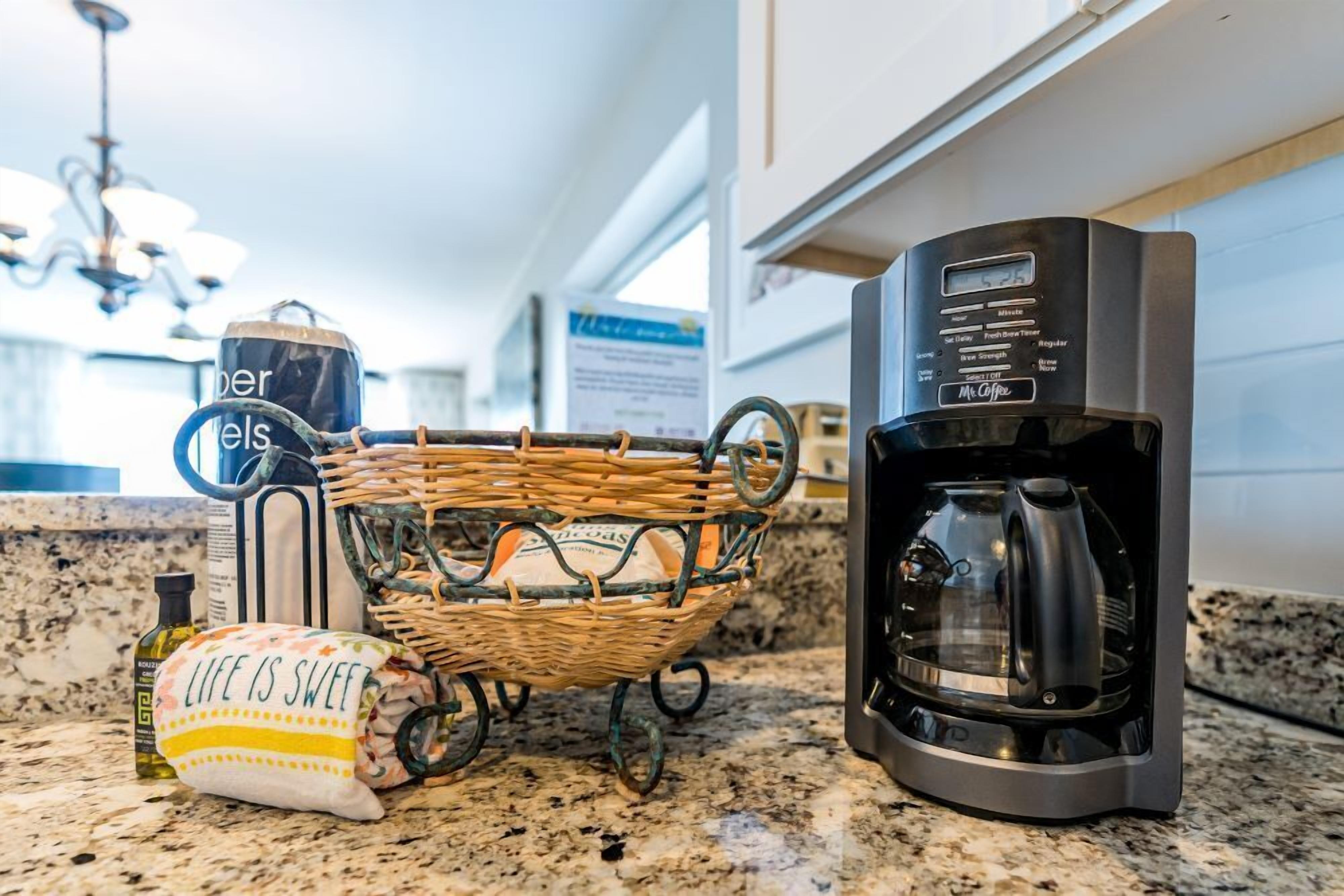 A kitchen counter with a coffee maker, a basket with a cloth, and a bottle of olive oil.