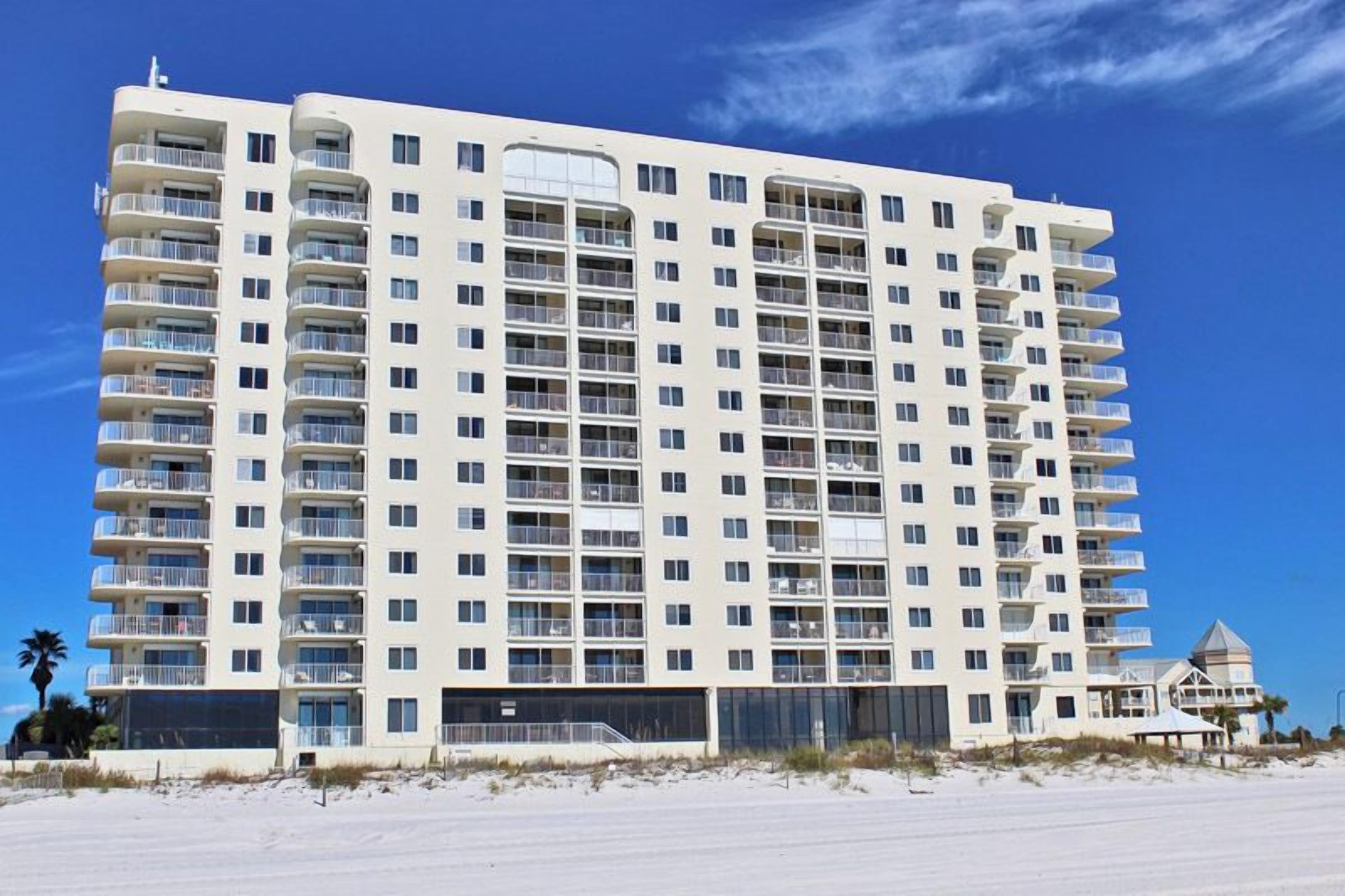 A multi-story hotel with balconies, a beach view, and a parking area.