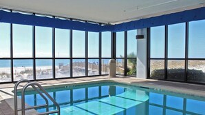 An indoor swimming pool with clear views of the beach and ocean through large windows.