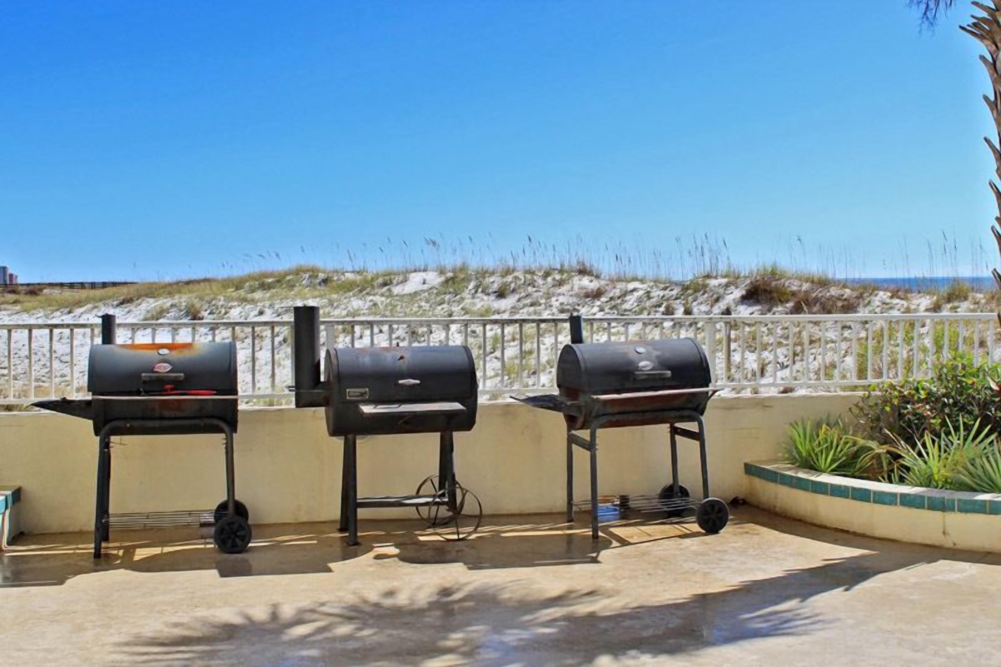 Tres parrillas de barbacoa en un patio con vistas a una playa arenosa y dunas.