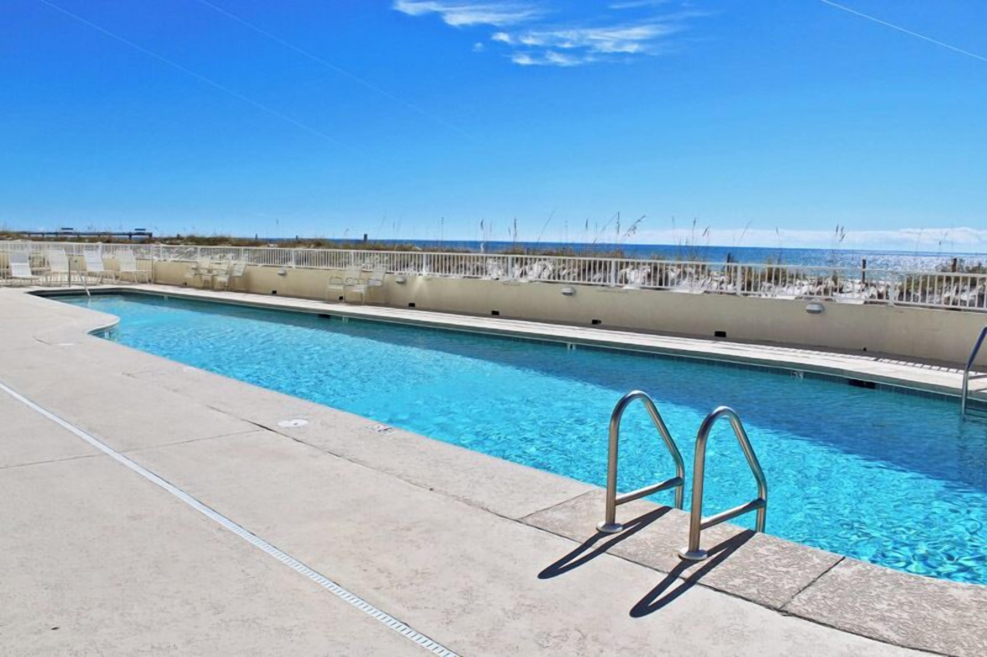 Une piscine rectangulaire à l’eau d’un bleu limpide, dotée d’une plage en béton et d’une échelle en métal.