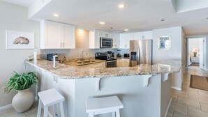A modern kitchen with white cabinets, granite countertops, a central island with stools, and stainless steel appliances.