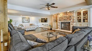 A spacious living room with a stone fireplace, leather sofas, and a ceiling fan. - Sunrise Beach Waterfront Estate Great for Families (Sunrise Beach)