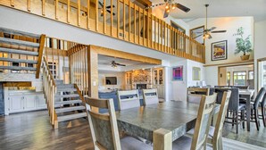 A spacious dining area with a large wooden table and chairs, a kitchen in the background, and a staircase leading to an upper level. - Sunrise Beach Waterfront Estate Great for Families (Sunrise Beach)