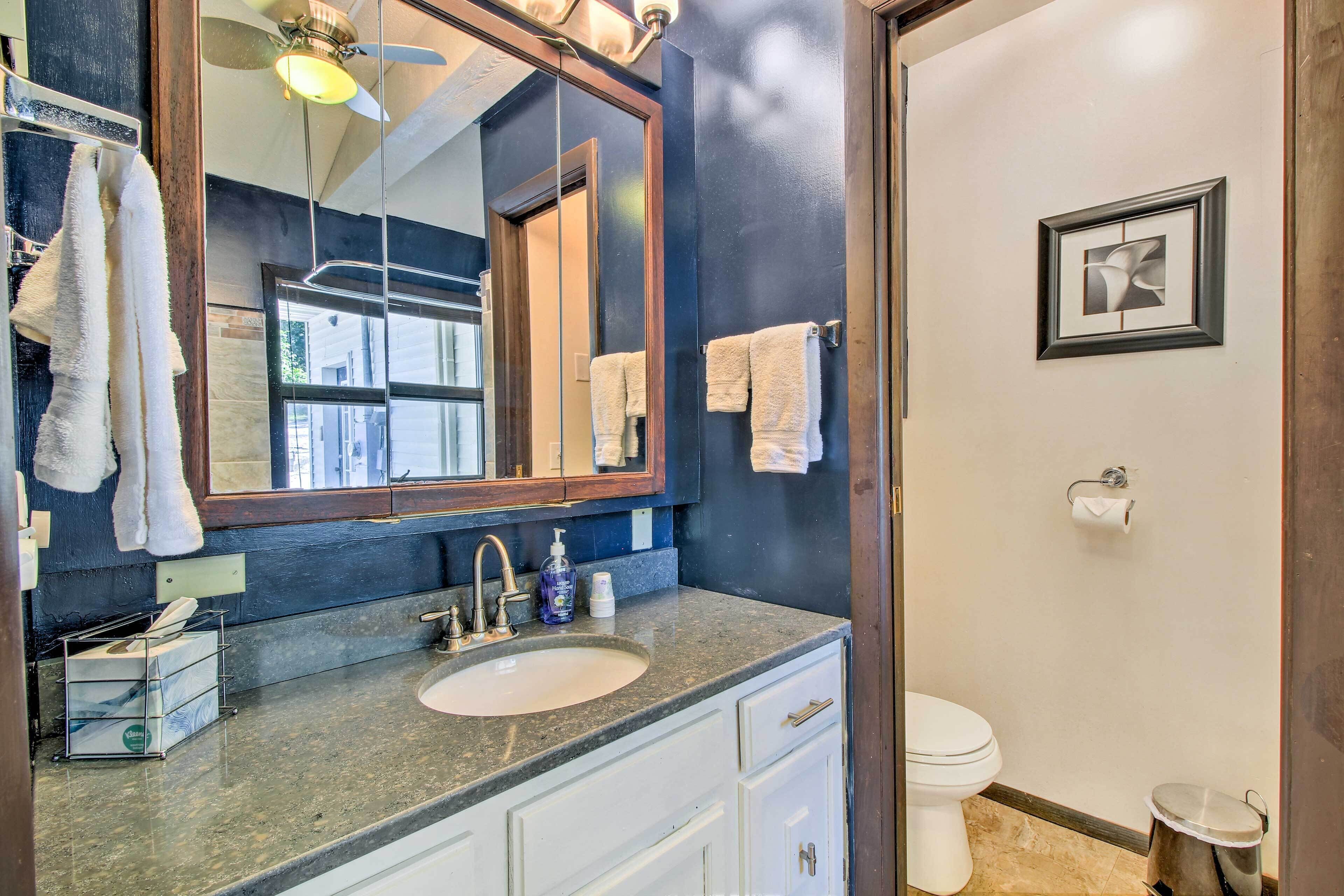 Une salle de bain avec un grand miroir, un lavabo, des toilettes et une poubelle.