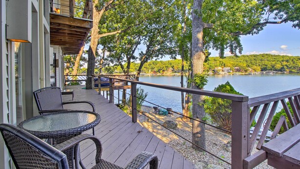 A wooden deck with wicker furniture overlooking a lake, surrounded by trees and a distant shoreline. - Sunrise Beach Waterfront Estate Great for Families (Sunrise Beach)