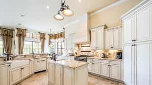 A spacious kitchen with white cabinetry, a large island, and a central island with a stove. - Je50286 - Reunion Resort - 5 Bed 5 Baths Villa (Kissimmee)