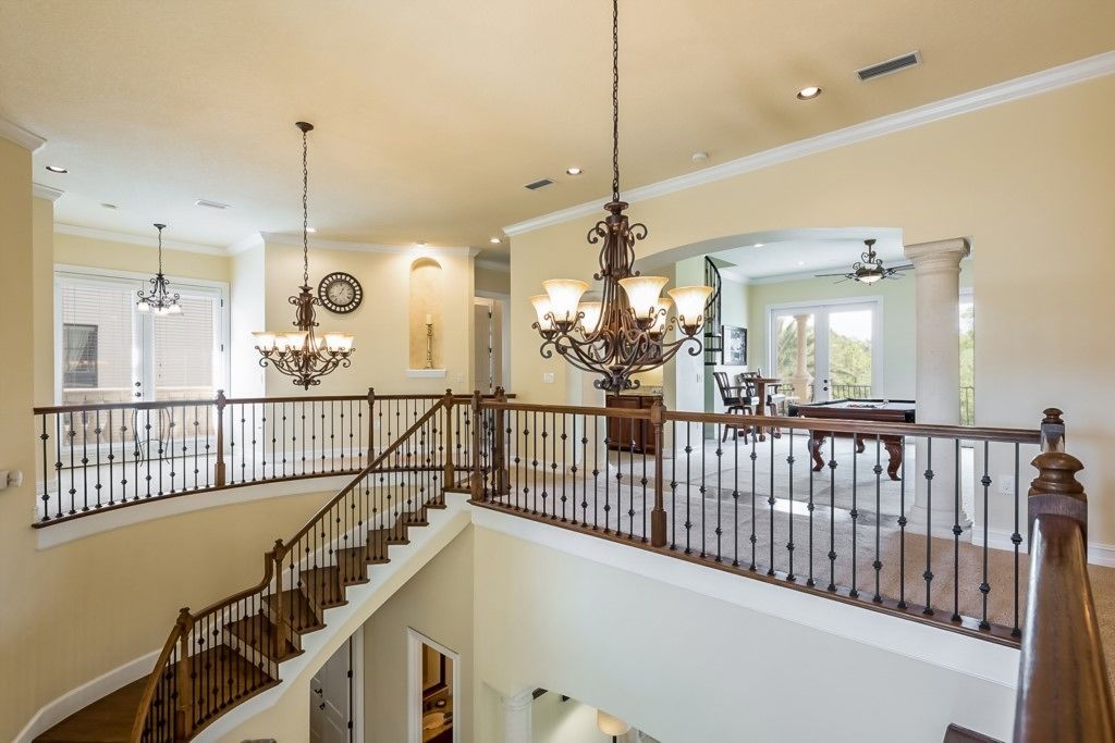 A spacious interior with a grand staircase, multiple chandeliers, and a large open living area with a view of the outdoors.