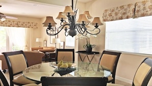 A dining area with a round glass table, six chairs, a chandelier, and a potted plant. - Je37919 - Reunion Resort - 4 Bed 4 Baths Villa (Kissimmee)