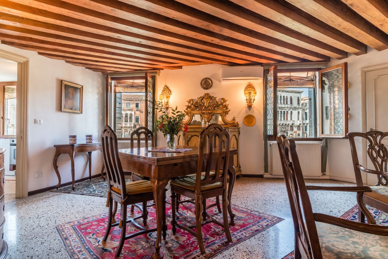 A dining area with a wooden table, chairs, and a patterned rug.