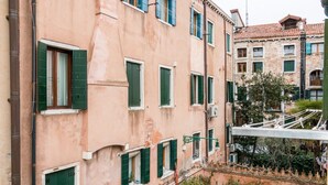 A multi-story building with green shutters, a visible balcony, and a street view with a tree and potted plants. - VIVALDI APARTMENT ON TWO LEVELS WITH ATTIC (Venezia)
