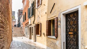 A narrow street with buildings on either side, featuring a mix of brick and plaster facades, and a wooden door with a metal gate. - VIVALDI APARTMENT ON TWO LEVELS WITH ATTIC (Venezia)