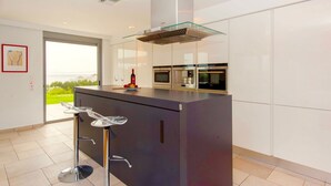 A modern kitchen with a central island, built-in oven, and a glass-top bar stool.