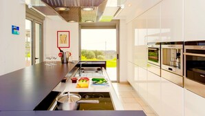 A modern kitchen with a glass-top island, stainless steel appliances, and a view of greenery outside.