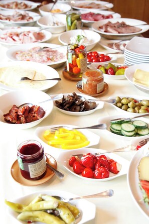 Una mesa con diversos alimentos y condimentos, como pepinos en rodajas, tomates cherry, aceitunas y un frasco de mermelada.